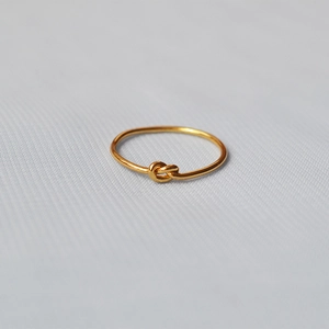 Minimalist handmade gold plated brass knot ring on a grey fabric background