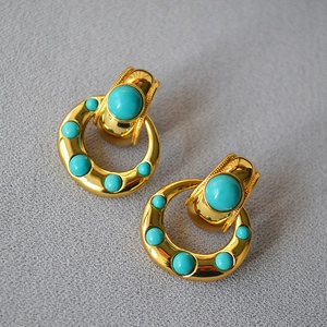 Macro shot of vintage gold-plated brass earrings with turquoise stones on dark fabric