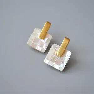 Detailed macro view of geometric earrings featuring iridescent mosaic mother of pearl inlay