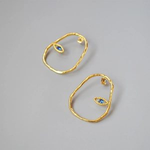 Detail view of gold-plated irregular eye earrings featuring vibrant blue zircon inlay