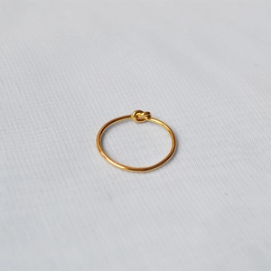 Macro detail of a handmade gold-plated brass wire knot ring on textured fabric