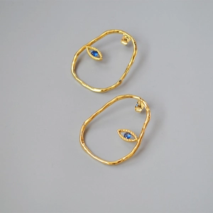 Detailed close-up of golden irregular textured earrings with blue evil eye stone inlay