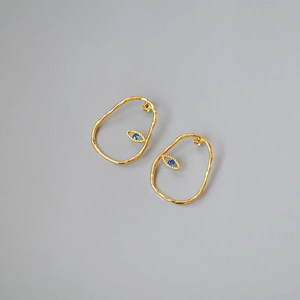 Detail view of gold-plated irregular hoop earrings with a blue evil eye stone accent