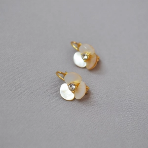 Macro detail of gold three-petal shell clover earrings with zircon center on grey fabric