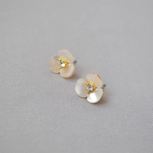 Close-up of golden clover stud earring with white shell petals and central crystal