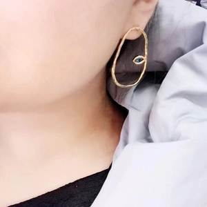 Minimalist gold irregular hoop earrings with blue evil eye stone worn by a model