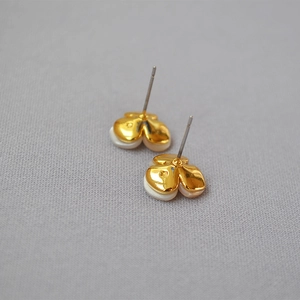 Close-up of gold clover earrings featuring white shell petals and silver needles