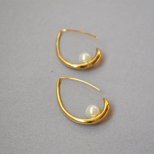 Detail of streamlined gold curved earrings with round white pearl inlays on fabric