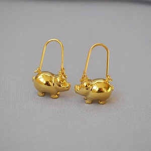 Close-up of polished gold-plated pig-shaped earrings on textured grey fabric