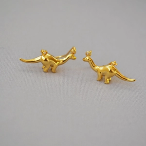 Close-up of gold-plated brass dinosaur earrings with a polished glossy finish