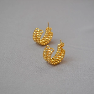 Detail of golden C-shaped hoop earrings with woven chain texture and polished finish