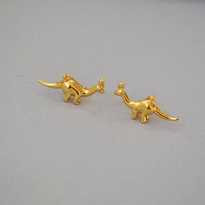 Macro shot of two polished gold-plated brass dinosaur pendants on a grey fabric background