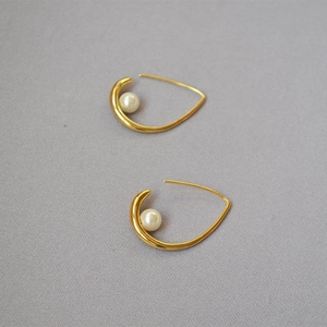 Macro detail of golden teardrop earrings featuring an inlaid pearl on grey fabric
