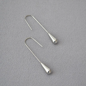 Detail view of mirror-finish silver teardrop drop earrings on a grey textured fabric