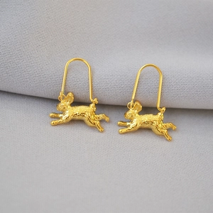 Macro shot of gold-plated rabbit earrings with detailed fur texture on grey fabric
