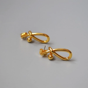 Macro shot of twisted knot gold stud earrings with polished finish and small bead detail
