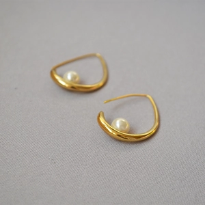 Macro detail of gold irregular hook earrings featuring a white round inlaid pearl