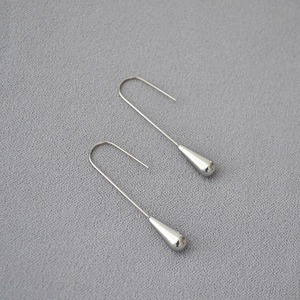 Close-up of polished silver teardrop earrings on a textured grey background surface