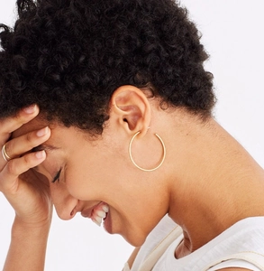 Close-up of a model wearing large minimalist golden hoop earrings in a polished brass finish