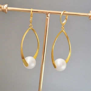 Detail of gold-plated brass teardrop earrings with white circular pearl on a display stand