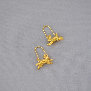 Detailed close-up of rabbit-shaped gold-plated earrings with matte texture on gray background