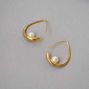 Close-up of golden teardrop hook earrings with polished finish and round white pearls
