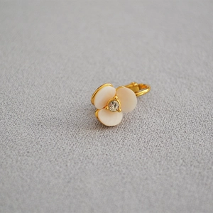 Detailed close-up of white shell clover earring with gold base and zircon center