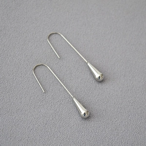 Detailed view of silver-plated brass teardrop earrings on grey textured fabric