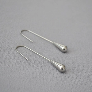 Macro detail of silver finish brass water drop earrings on textured gray background