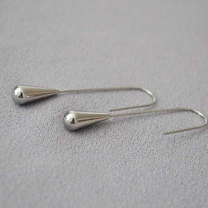 Macro detail of polished silver teardrop earrings on a grey textured fabric background