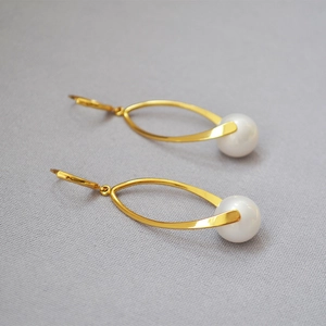 Detail of elegant gold arc earrings featuring high-luster white pearls on a minimalist fabric