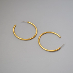 Macro view of matte gold C-shaped hoop earrings with a fine satin finish texture