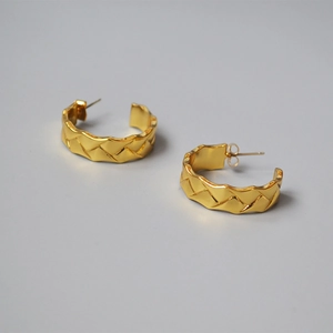 Macro view of woven textured gold hoop earrings featuring geometric lattice patterns