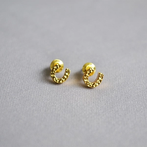 Detailed view of golden horseshoe studs with hand-hammered texture and polished finish