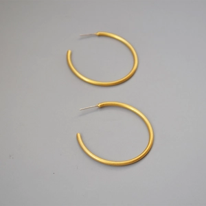 Macro shot of matte gold brass C-shaped hoop earrings with minimalist brushed metal finish