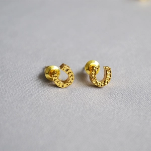 Close-up of golden horseshoe earrings with hand-hammered texture and metallic backing