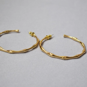 Detail of polished gold bamboo-style hoop earrings on a grey fabric texture background