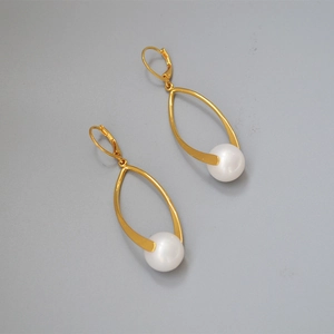 Detailed close-up of gold-plated drop earrings featuring large white pearls and French hooks