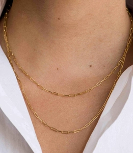 Detail of layered gold paperclip chain necklace styled on model with a white shirt