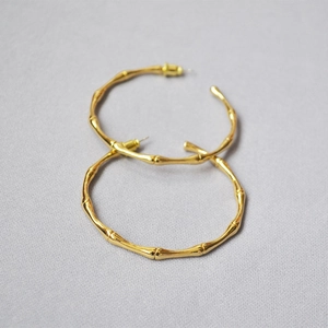 Macro shot of large golden bamboo-textured hoop earrings on light gray textured fabric