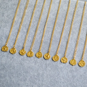 Detail of vintage gold zodiac coin necklaces with textured relief on soft grey velvet