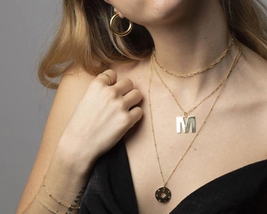 Detail of layered gold choker necklaces with M-letter and star pendants on a model