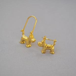 Detail of creative dog-shaped brass gold earrings with textured matte finish on fabric