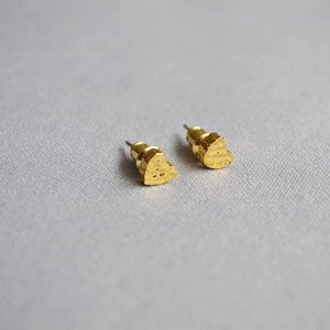 Macro view of gold heart stud earrings with unique hammered texture on fabric background
