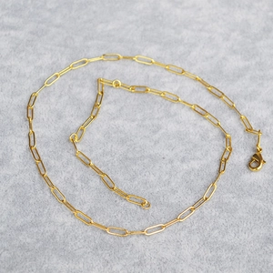 Detail of a golden paperclip chain necklace with a lobster clasp on a grey felt background