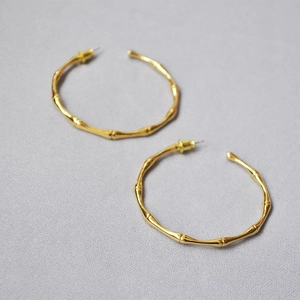 Detailed view of gold-plated bamboo textured hoop earrings on gray fabric