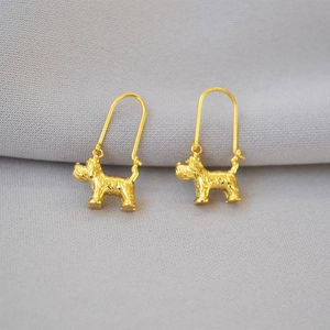 Macro detail of gold plated dog dangle earrings with textured finish on grey fabric