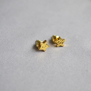 Macro detail of gold star earrings showing vintage hammered texture on fabric background