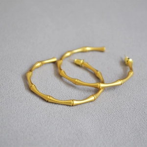 Close-up of bamboo-style gold hoop earrings with a matte texture on grey fabric