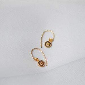 Détail de boucles d'oreilles œil porte-bonheur dorées avec zircons bleus sur tissu